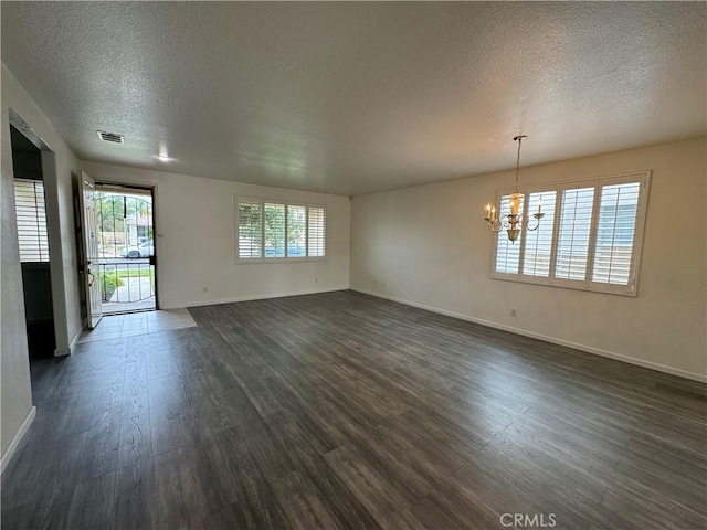 unfurnished room featuring dark wood-type flooring, a textured ceiling, and a notable chandelier