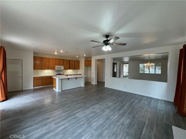 unfurnished living room with ceiling fan with notable chandelier, a textured ceiling, and dark wood-type flooring