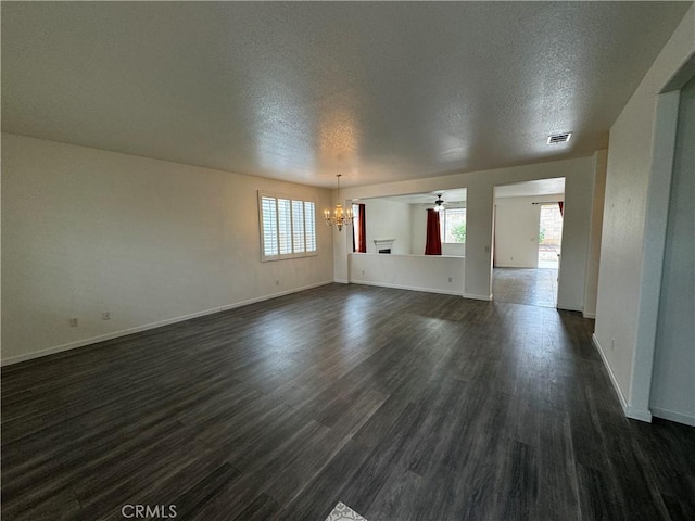 spare room with ceiling fan with notable chandelier, a textured ceiling, and dark wood-type flooring