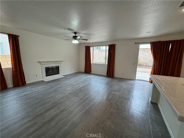 unfurnished living room with a tile fireplace, ceiling fan, dark hardwood / wood-style floors, and a textured ceiling