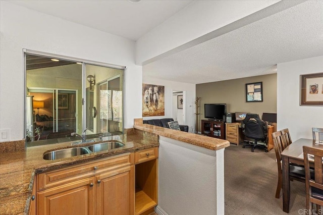 kitchen featuring kitchen peninsula, dark colored carpet, dark stone counters, a textured ceiling, and sink