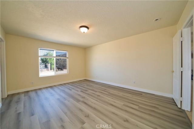 unfurnished room with a textured ceiling and light wood-type flooring