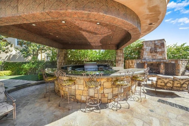 view of patio featuring an outdoor stone fireplace, a bar, an outdoor kitchen, and area for grilling