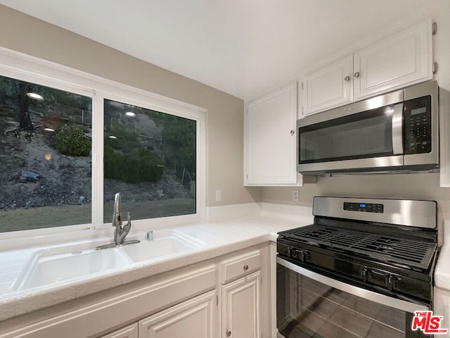 kitchen with appliances with stainless steel finishes, tile patterned floors, sink, tile countertops, and white cabinets