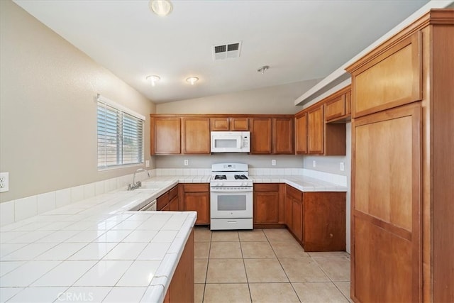 kitchen featuring vaulted ceiling, light tile patterned flooring, white appliances, tile counters, and sink