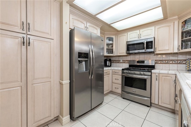 kitchen featuring tile countertops, decorative backsplash, light tile patterned flooring, and appliances with stainless steel finishes