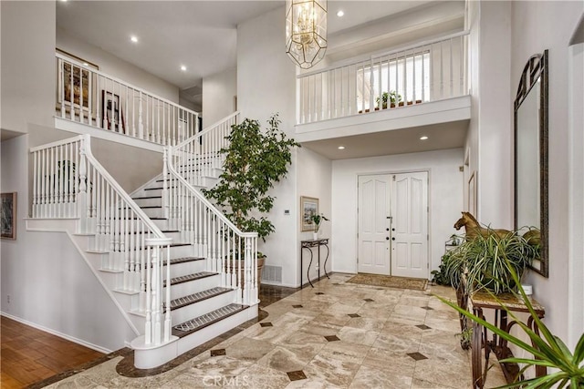 foyer with a towering ceiling, wood-type flooring, and a notable chandelier