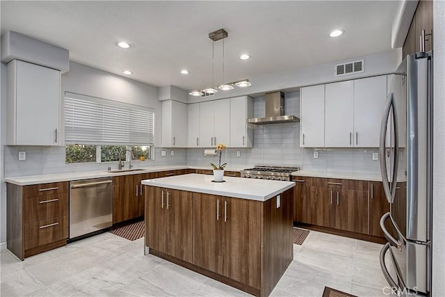 kitchen with white cabinets, wall chimney exhaust hood, a kitchen island, and stainless steel appliances