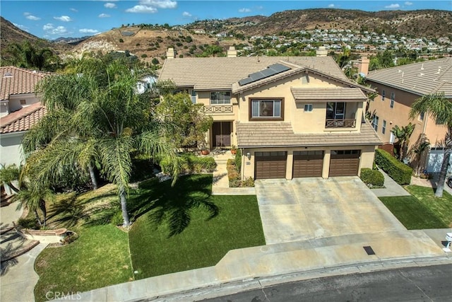 view of front facade with solar panels, a mountain view, a front yard, and a garage