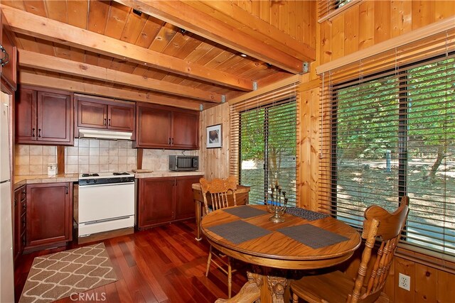 kitchen with white range oven, dark wood-type flooring, tasteful backsplash, wood walls, and beamed ceiling