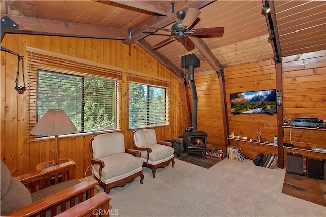 sitting room with a wood stove, carpet flooring, wooden walls, vaulted ceiling with beams, and a ceiling fan