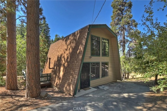 view of property exterior featuring a patio, a gambrel roof, and a shingled roof
