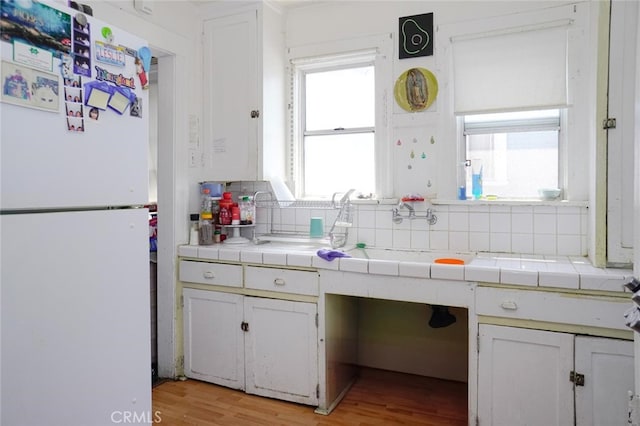 kitchen with light hardwood / wood-style flooring, tile countertops, white fridge, and decorative backsplash