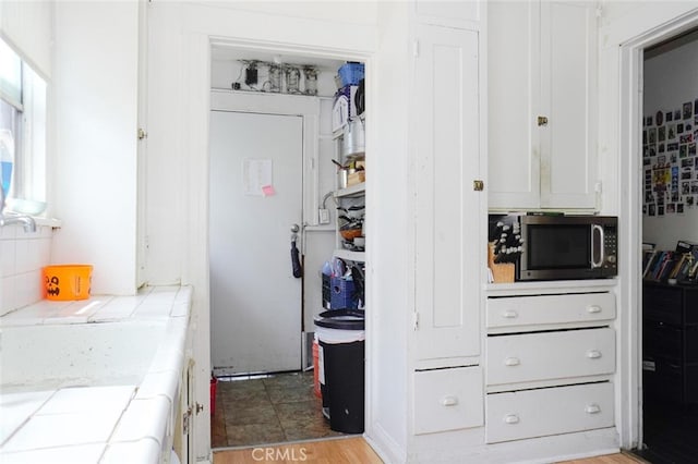 interior space with white cabinets, backsplash, light hardwood / wood-style floors, and tile counters