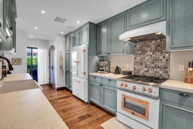 kitchen with sink, backsplash, dark hardwood / wood-style floors, gas range, and white fridge