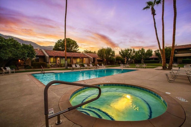 pool at dusk featuring a community hot tub and a patio