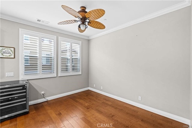 empty room featuring crown molding, dark hardwood / wood-style flooring, ceiling fan, and wine cooler