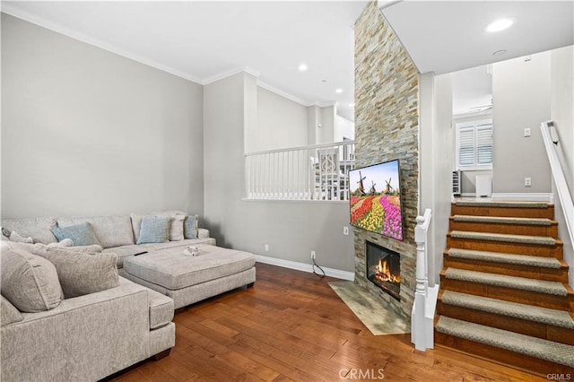 living room with wood-type flooring, a stone fireplace, and ornamental molding