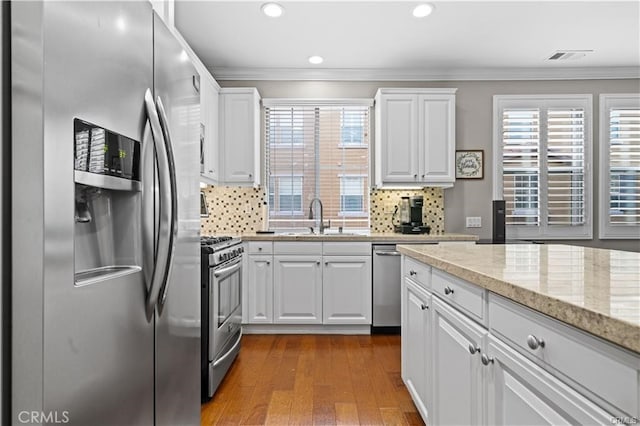 kitchen with wood-type flooring, sink, white cabinetry, appliances with stainless steel finishes, and ornamental molding