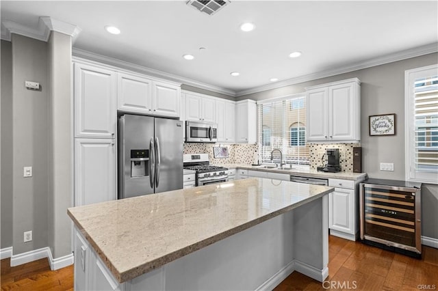 kitchen with beverage cooler, white cabinets, appliances with stainless steel finishes, and a center island