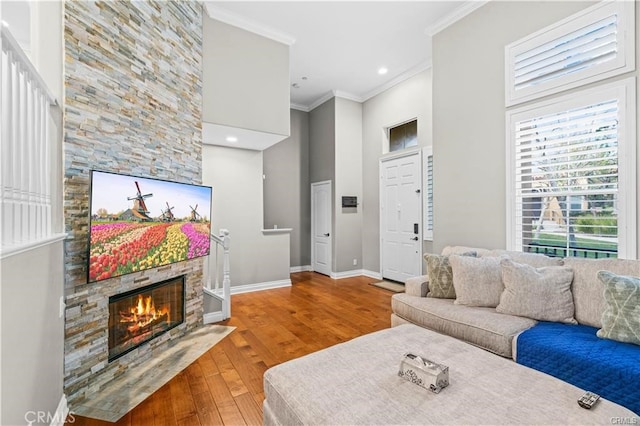 living room with a high ceiling, a fireplace, ornamental molding, and hardwood / wood-style floors