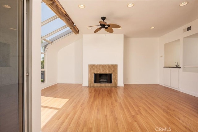 unfurnished living room with a tile fireplace, ceiling fan, light hardwood / wood-style flooring, and sink