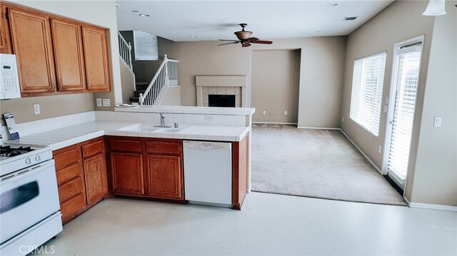 kitchen with ceiling fan, kitchen peninsula, sink, white appliances, and tile countertops