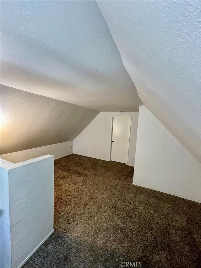 bonus room featuring dark colored carpet, lofted ceiling, and a textured ceiling