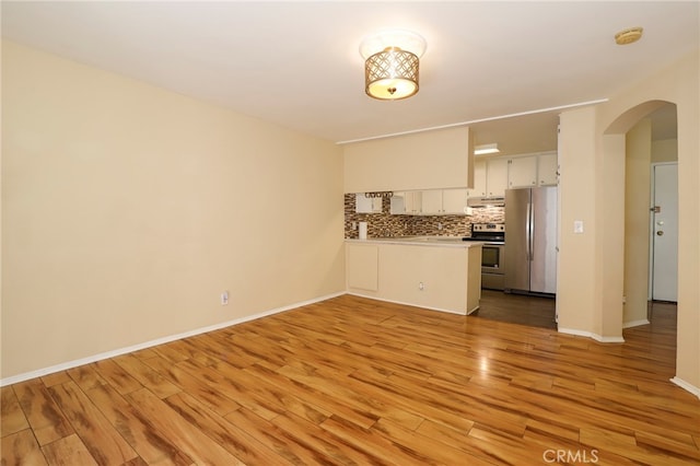 kitchen featuring white cabinets, kitchen peninsula, tasteful backsplash, stainless steel appliances, and light hardwood / wood-style floors