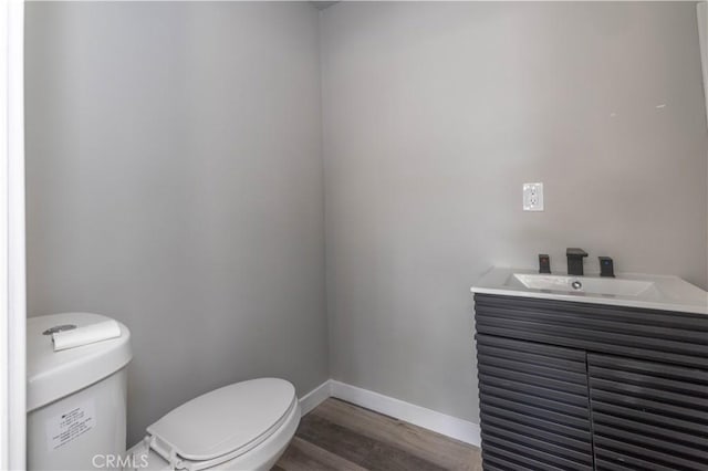 half bath with wood finished floors, a sink, toilet, and baseboards