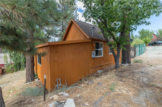 view of home's exterior with a shingled roof and fence