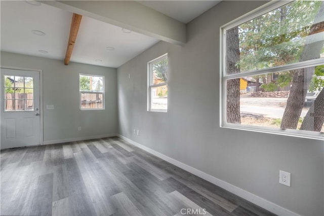 unfurnished room with baseboards, beam ceiling, and wood finished floors