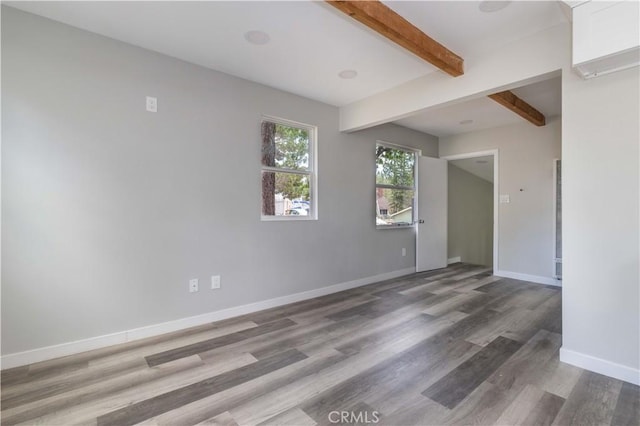 empty room featuring beam ceiling, baseboards, and wood finished floors