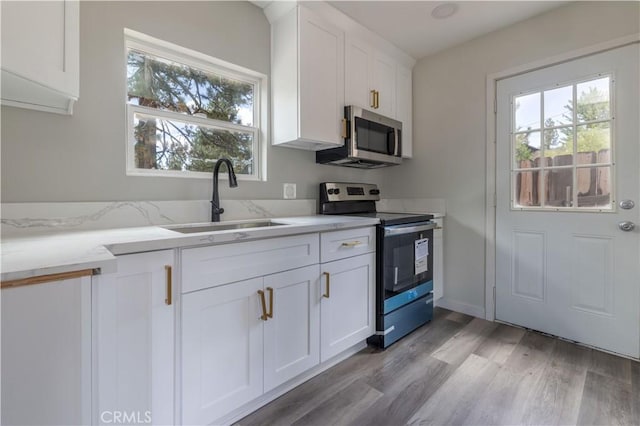 kitchen featuring stainless steel appliances, a sink, light wood-style floors, white cabinets, and light stone countertops