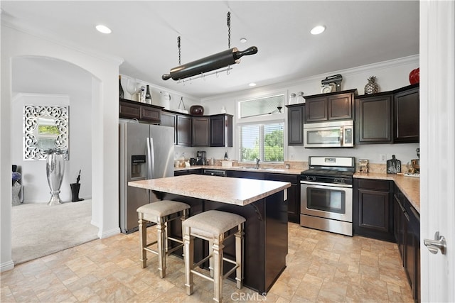 kitchen featuring appliances with stainless steel finishes, dark brown cabinets, a kitchen island, and a breakfast bar area