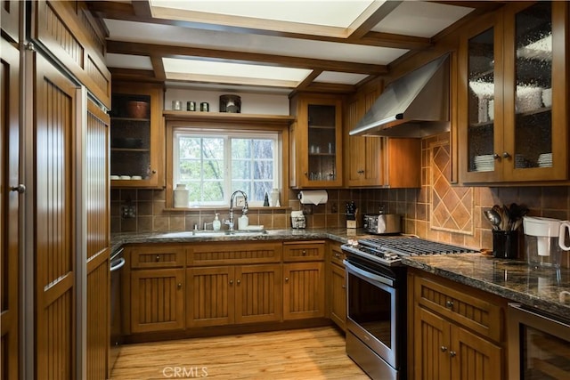 kitchen featuring wine cooler, sink, extractor fan, stainless steel gas range oven, and dark stone countertops