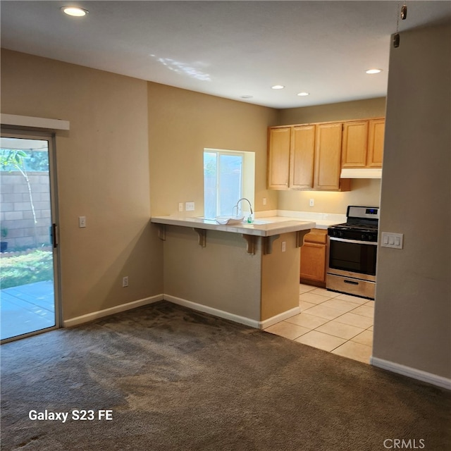 kitchen featuring stainless steel range with gas cooktop, a kitchen breakfast bar, light carpet, and kitchen peninsula