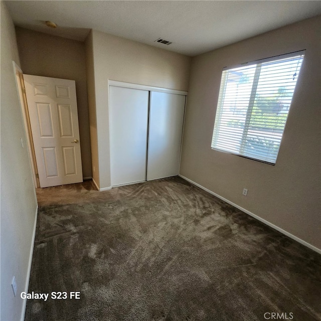 unfurnished bedroom featuring dark carpet and a closet