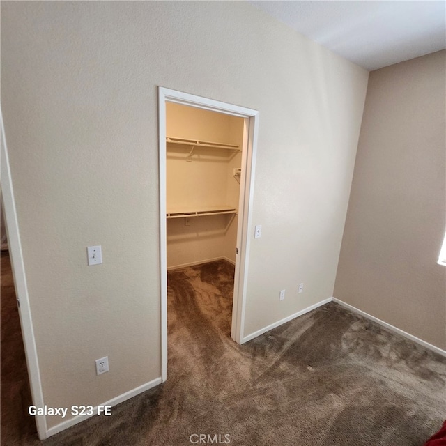 unfurnished bedroom featuring a closet, a spacious closet, and dark carpet