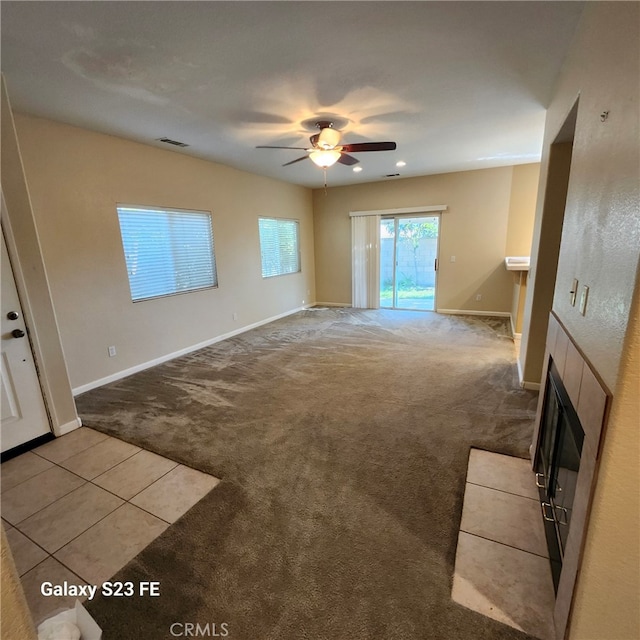 unfurnished living room featuring ceiling fan, light colored carpet, and a tiled fireplace