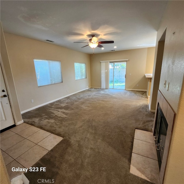 unfurnished living room featuring ceiling fan, light colored carpet, and a tiled fireplace