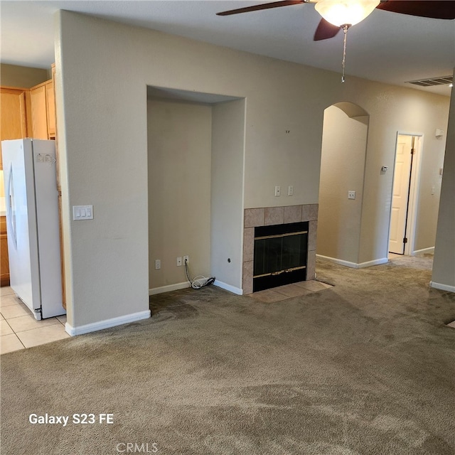 unfurnished living room featuring ceiling fan, light colored carpet, and a tile fireplace