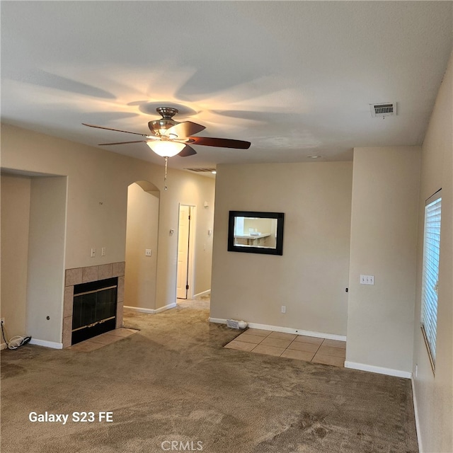 unfurnished living room with light carpet, ceiling fan, and a tile fireplace