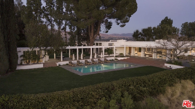 back house at dusk with a lawn and a patio area