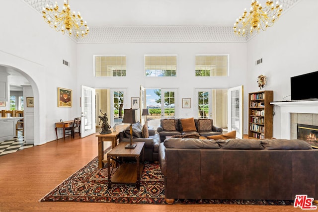 living room with wood-type flooring, a towering ceiling, and a tiled fireplace