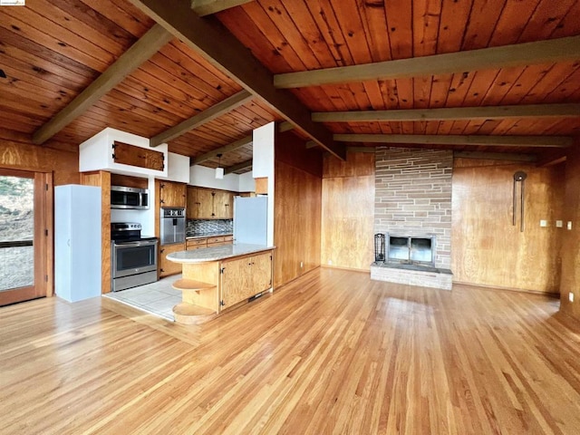 kitchen featuring stainless steel appliances, a stone fireplace, kitchen peninsula, wooden walls, and light wood-type flooring