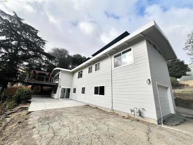 view of property exterior with a garage, a patio area, and a wooden deck