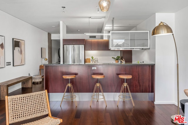 kitchen featuring a kitchen breakfast bar, kitchen peninsula, dark wood-type flooring, and stainless steel fridge