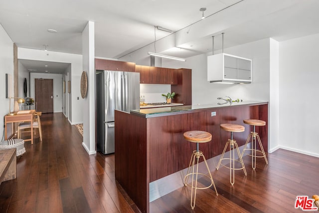 kitchen featuring dark hardwood / wood-style floors, a breakfast bar area, white cabinets, kitchen peninsula, and stainless steel fridge