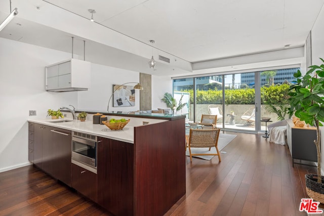 kitchen featuring sink, kitchen peninsula, dark brown cabinets, dark hardwood / wood-style floors, and stainless steel microwave